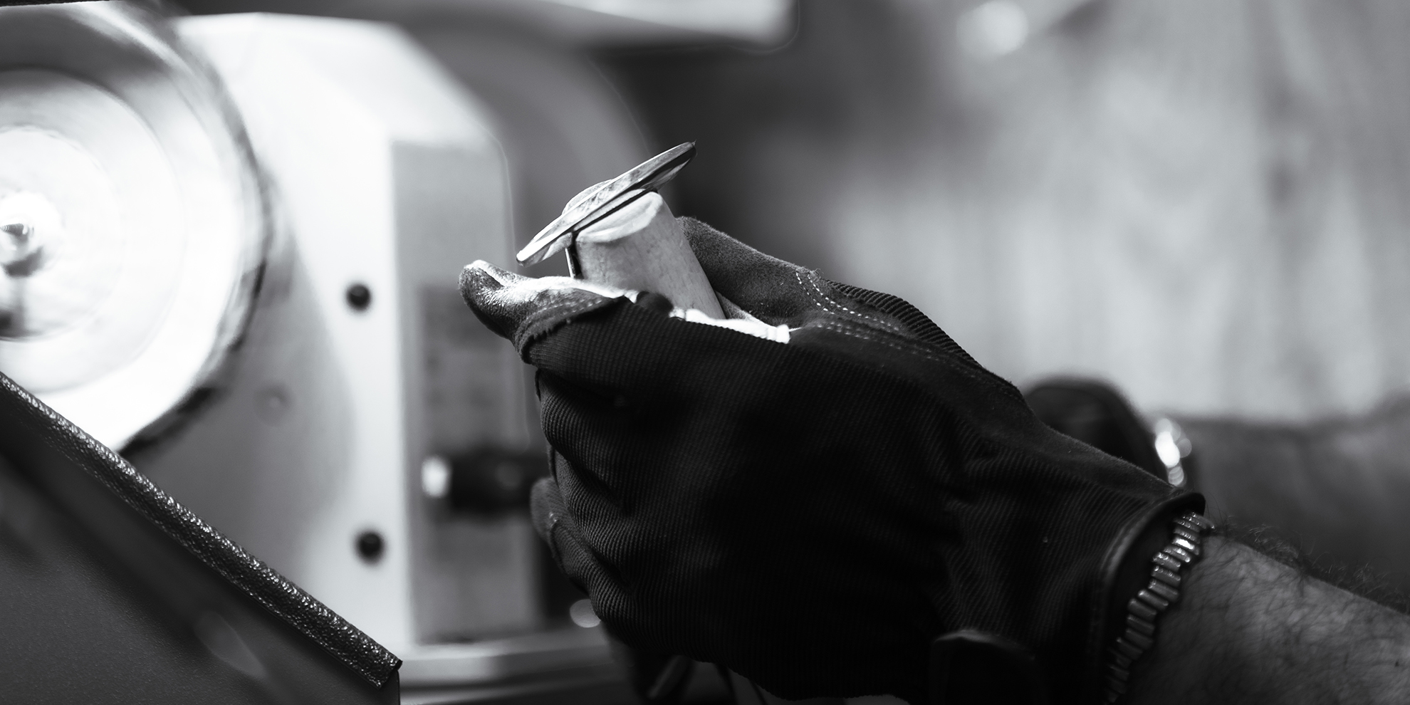 Close-up of an artisan's hands carefully applying a chamfer to a silver jewelry piece, with light reflecting off the precise bevel.